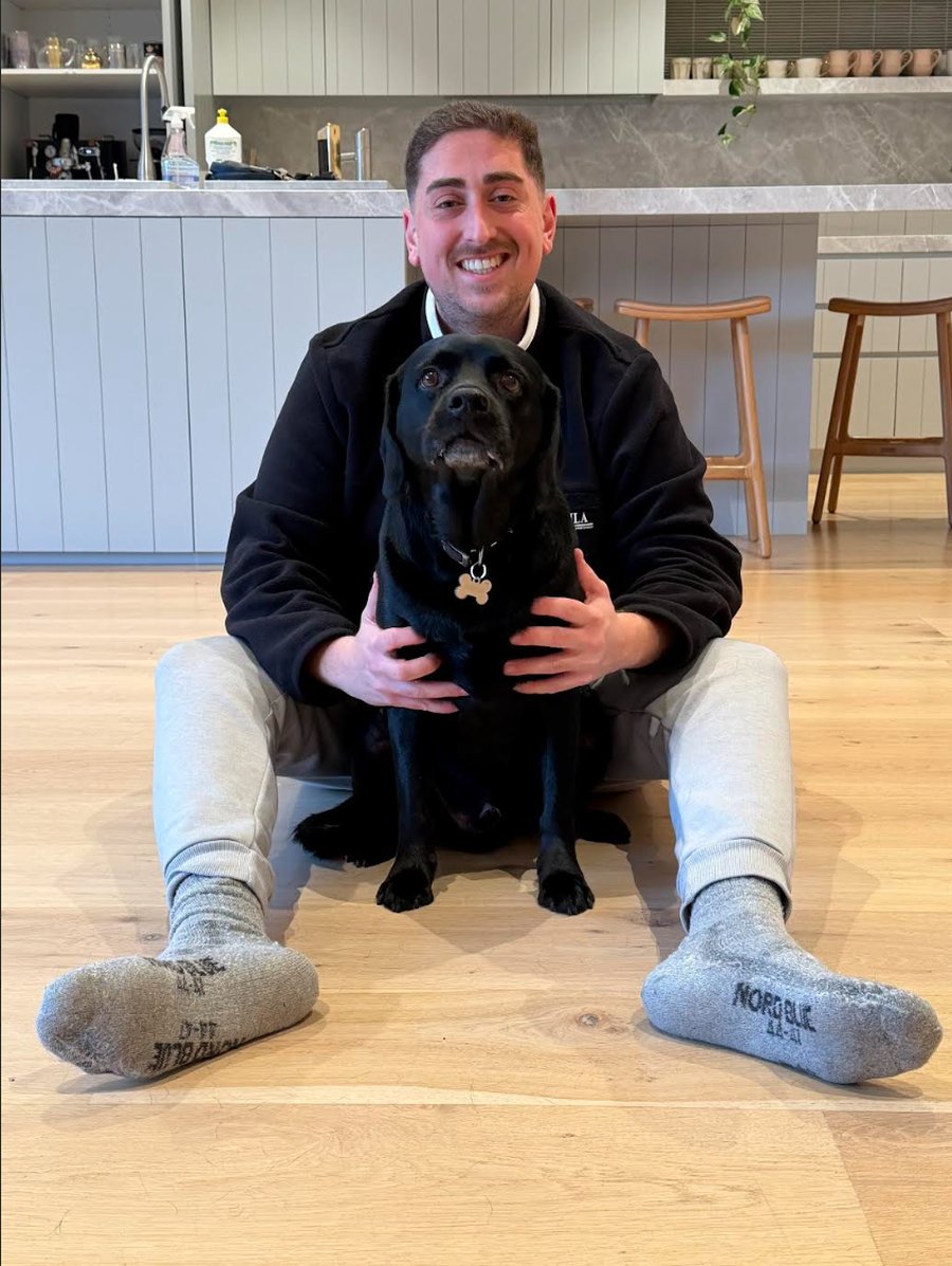 Gabe, Heeling Dogs trainer, sitting with a client's black Labrador during an in-home session in Melbourne